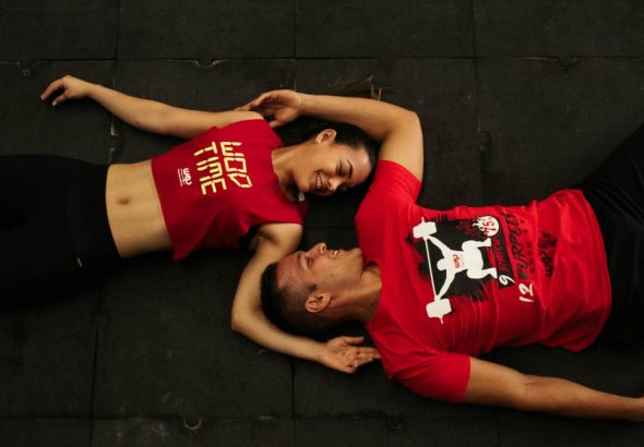 A man and woman relaxing on gym floor in Colombia, wearing matching red workout clothes.